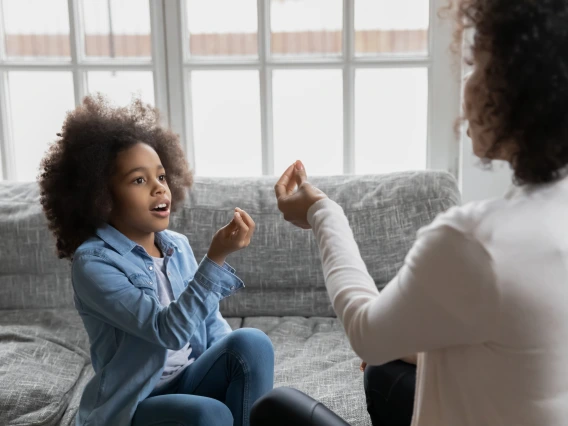 Close up African American mother teaching disabled daughter, showing symbols, little girl practicing sign language, repeating sounds, involved in speaking lesson with teacher at home, hearing loss